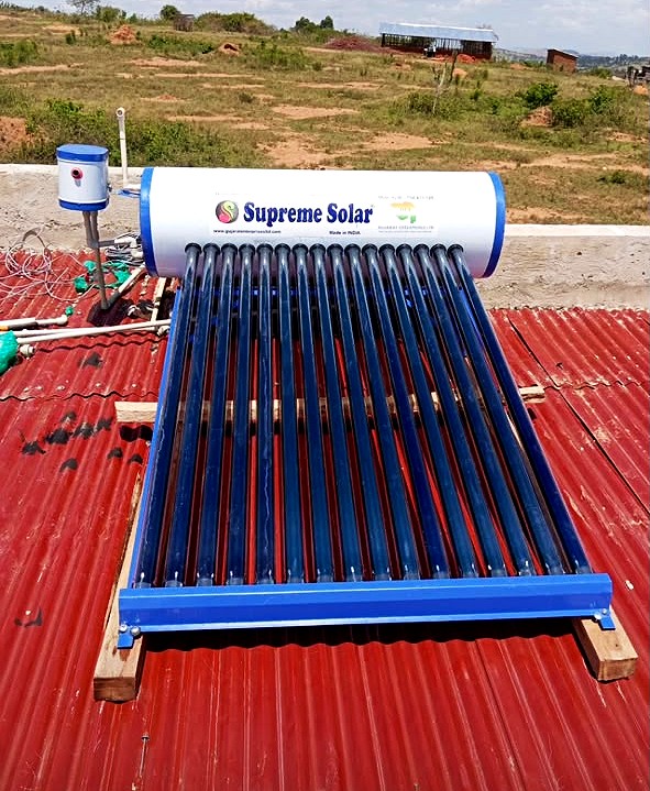 A solar water heater with blue evacuated tubes on a red iron sheet roof